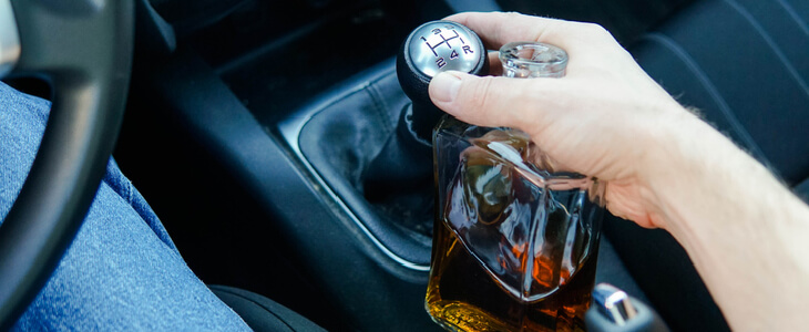 Man driving a car while holding an alcoholic drink