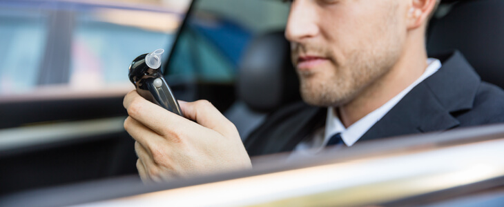 Man breathing into an ignition interlock device in his car