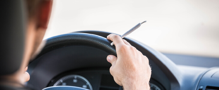 Young man driving his car while smoking a Marijuana cigarette