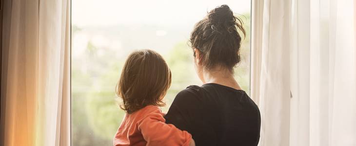 Young mother holding her daughter while staring out a window