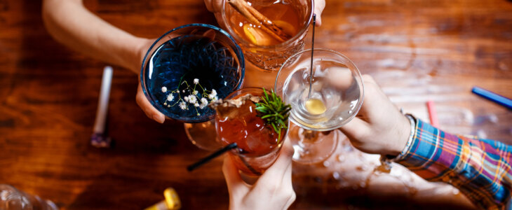 friends clinking by glasses with various alcoholic cocktails at table,close up top view