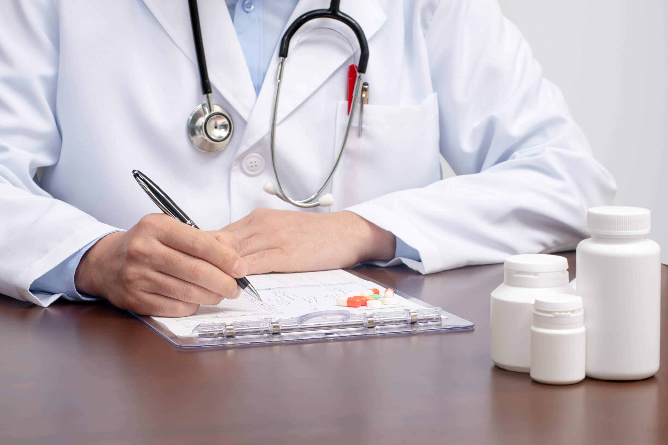 A male doctor writing on the medical form with the stethoscope nearby