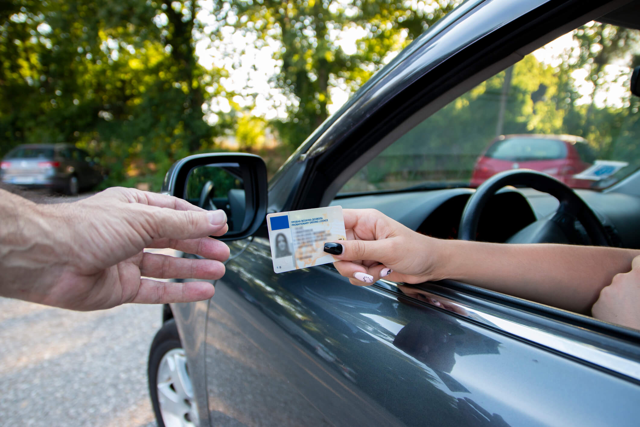 Teenager driver commited a minor offence and handing over her licence to a police officer reaching towards the open window.Police officer controlling traffic on the road