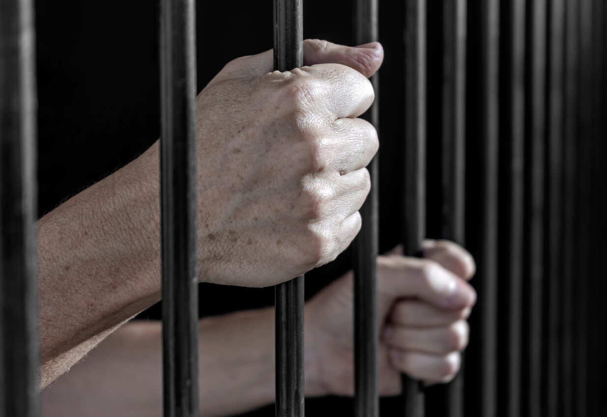 Prisoner's hands gripping the bars of a cell in jail. Serving of prison sentences for committing crimes.